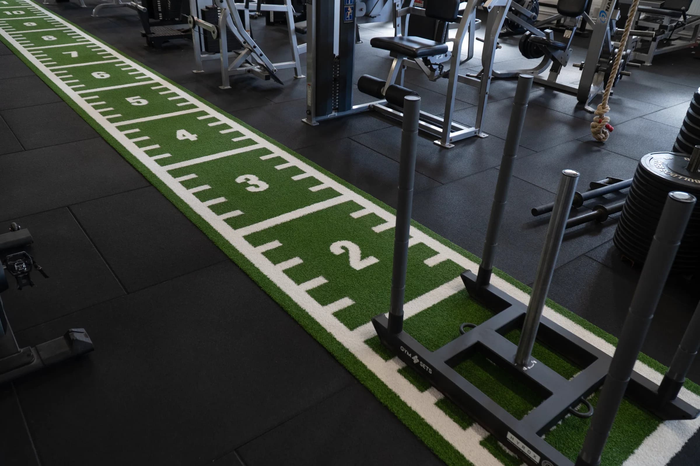 Numbered indoor turf lane with a weighted training sled and resistance equipment at VK Gym.